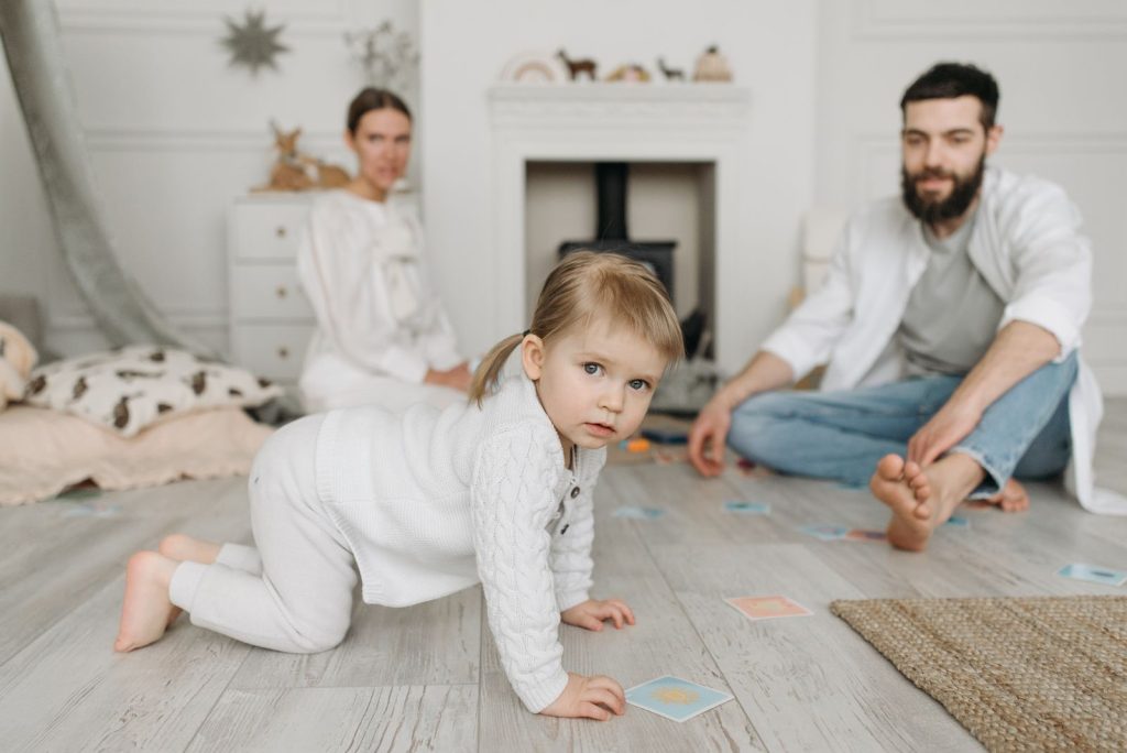 Toddler crawling on the floor while parents sit nearby