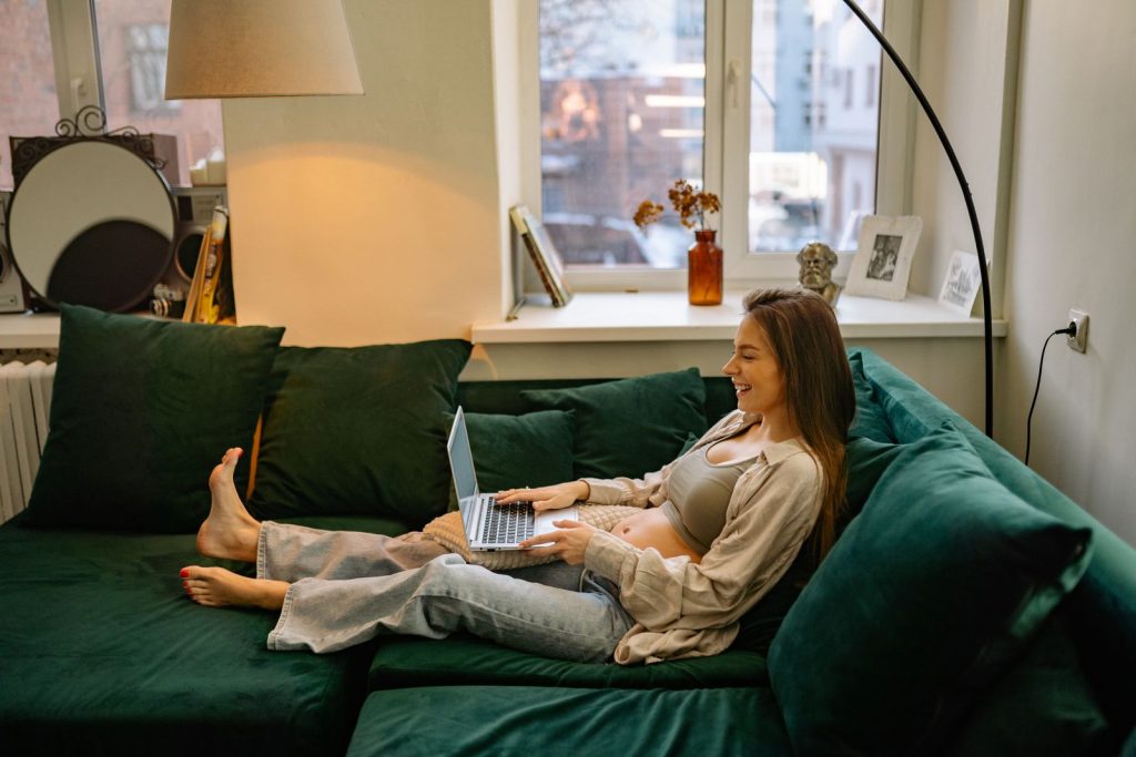 Pregnant woman on a green sofa working on a laptop