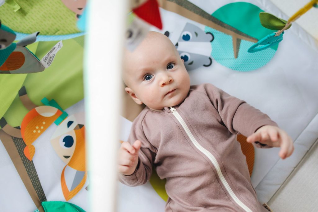 Baby lying under a wooden play gym