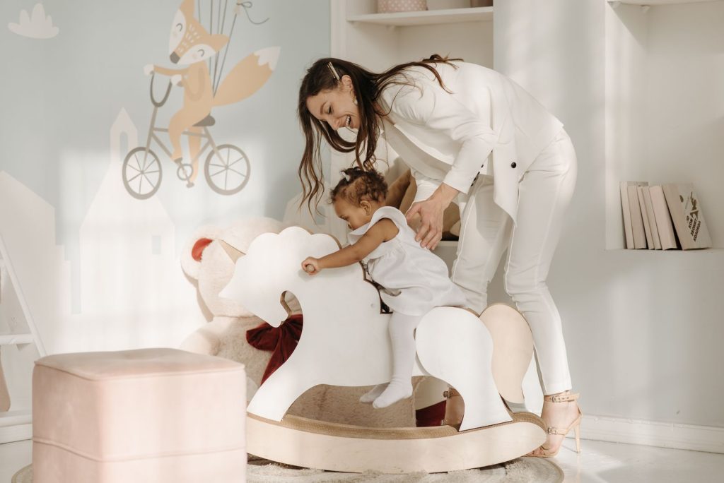 Mother steadying a toddler on a rocking horse in a white room