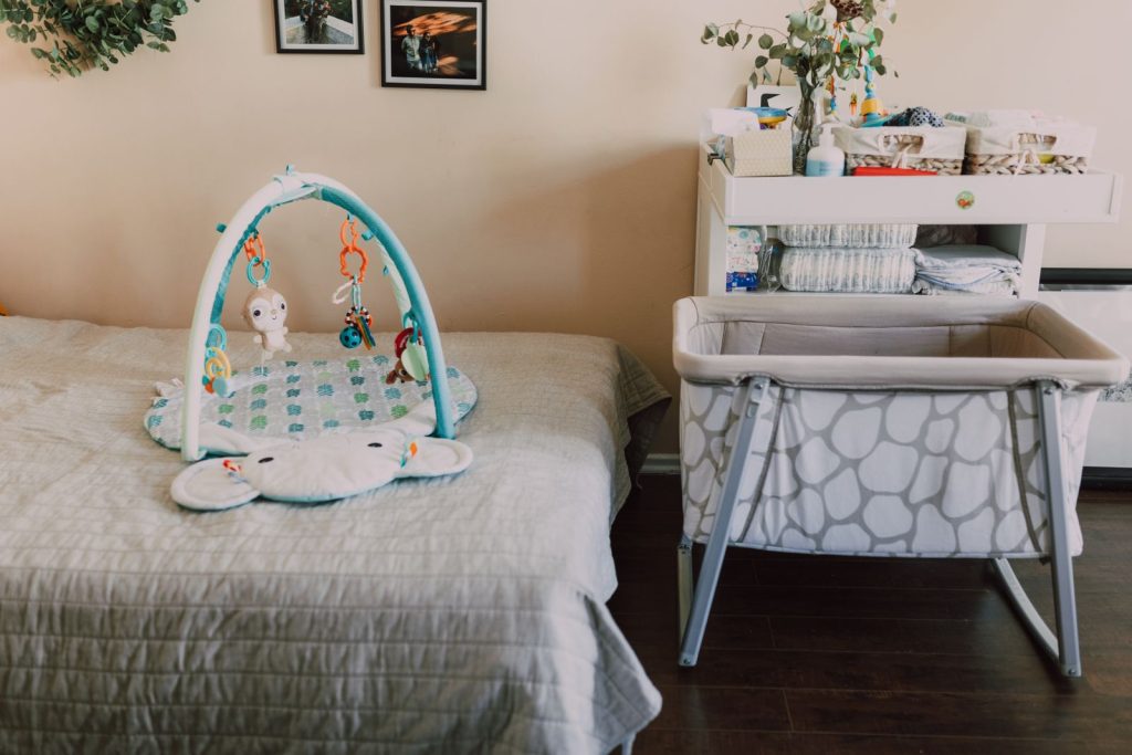Empty bassinet beside a bed, with a play mat on the covers
