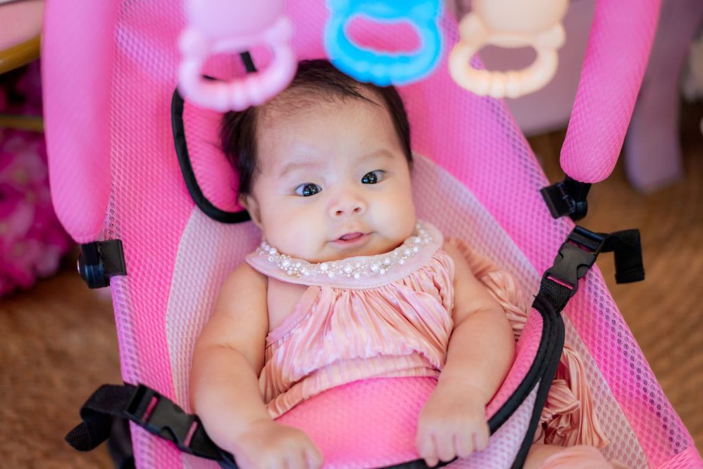 Baby buckled into a pink bouncer seat with a toy bar