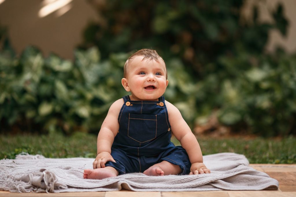 Baby in denim overalls sitting up on a blanket outdoors