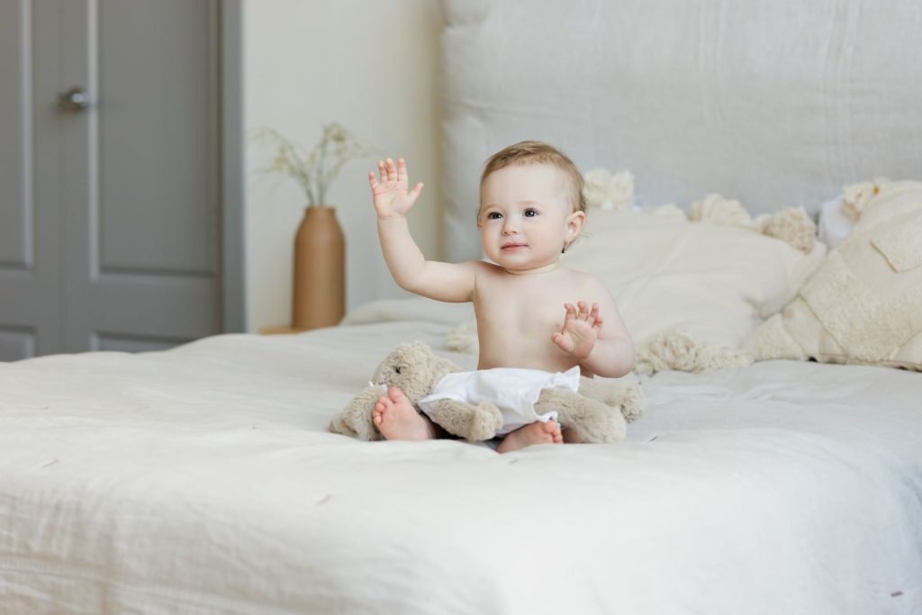Baby sitting up on a white bed