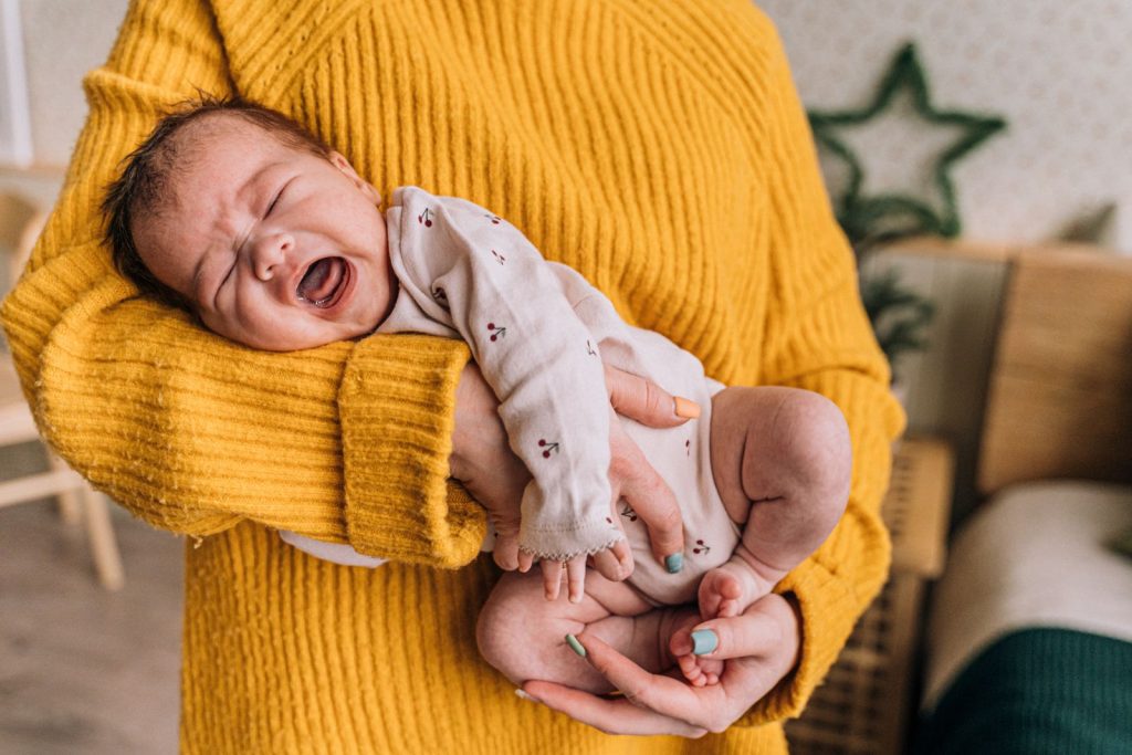 Parent in a yellow sweater comforting a crying baby