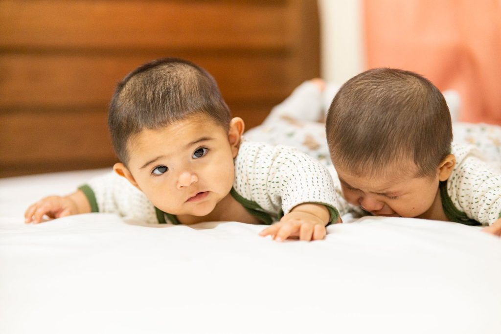 Twin babies lying side by side on a bed