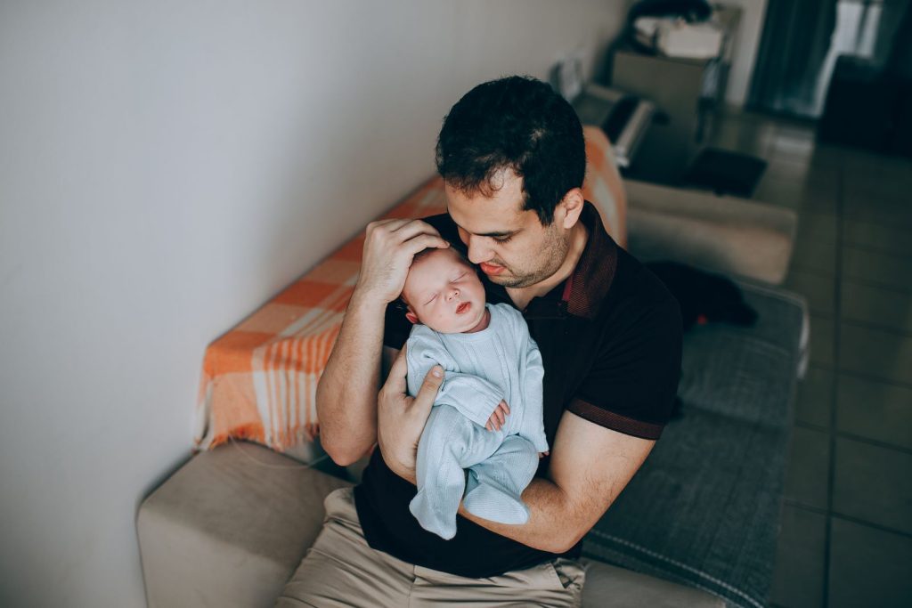 Father sitting on a sofa holding his newborn