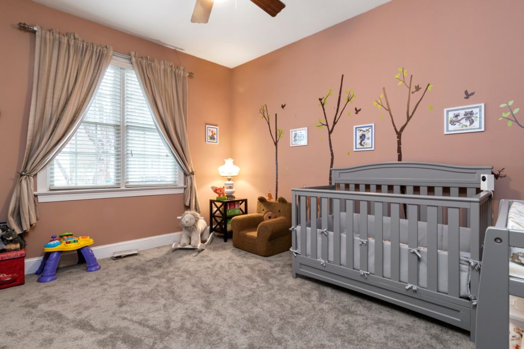Nursery with terracotta walls, a gray crib and tree wall decals
