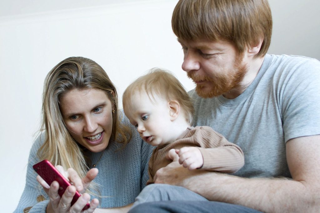 Parents holding their baby while looking at a smartphone