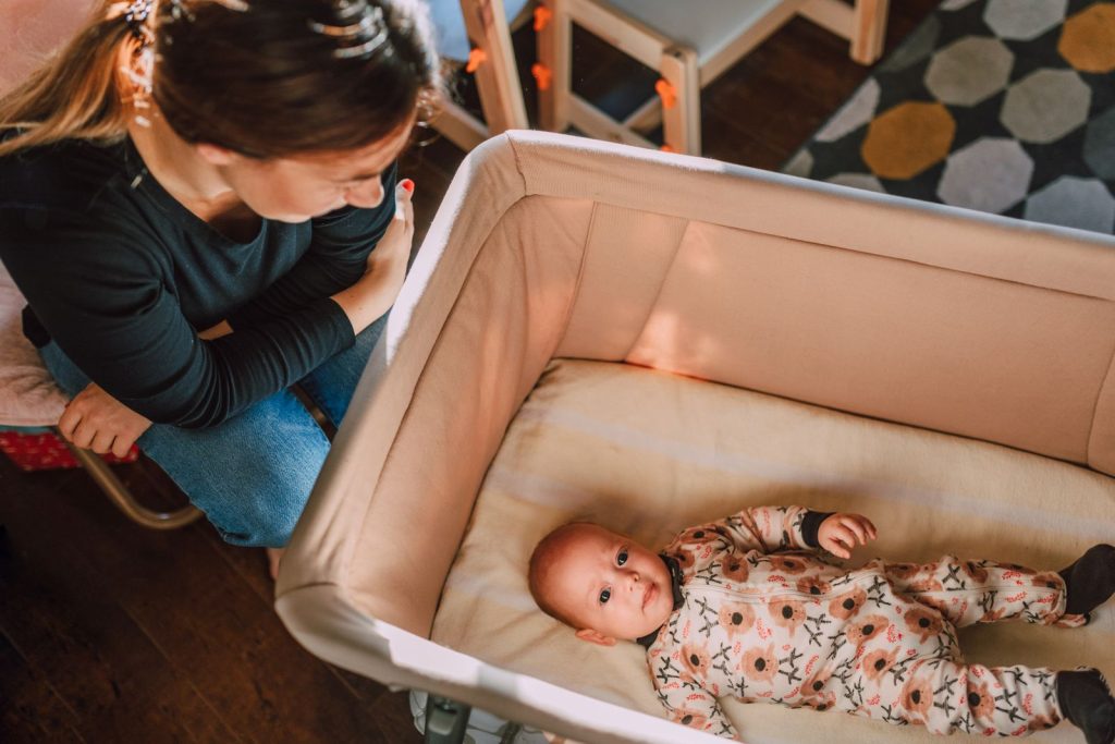 Mother watching her baby lying awake on its back in a bassinet