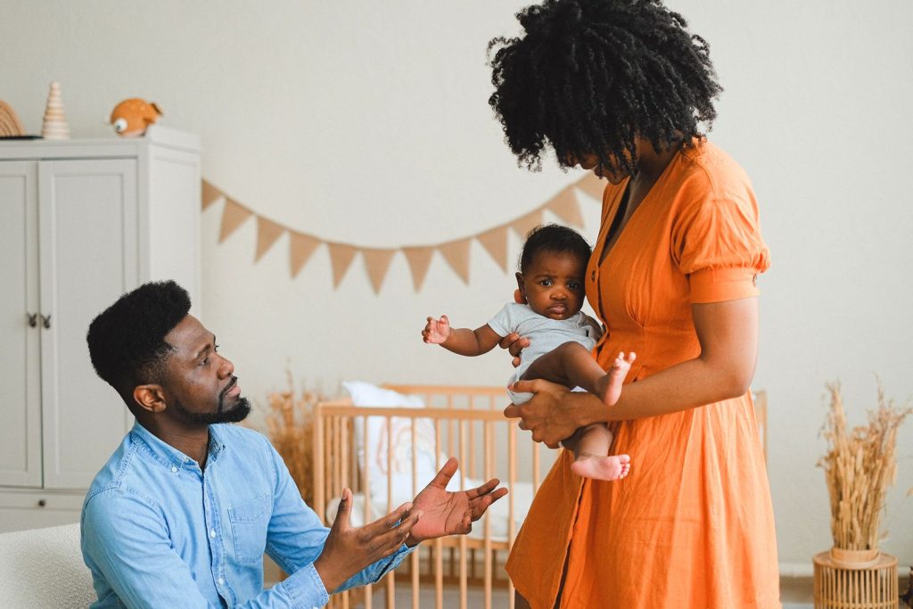 Parents with their baby in a bright nursery with a wooden crib and bunting on the wall