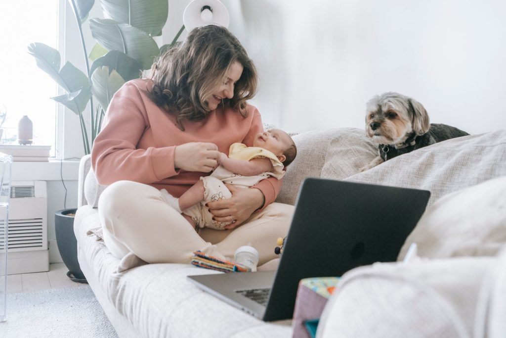 Mother holding her baby while using a laptop on a sofa