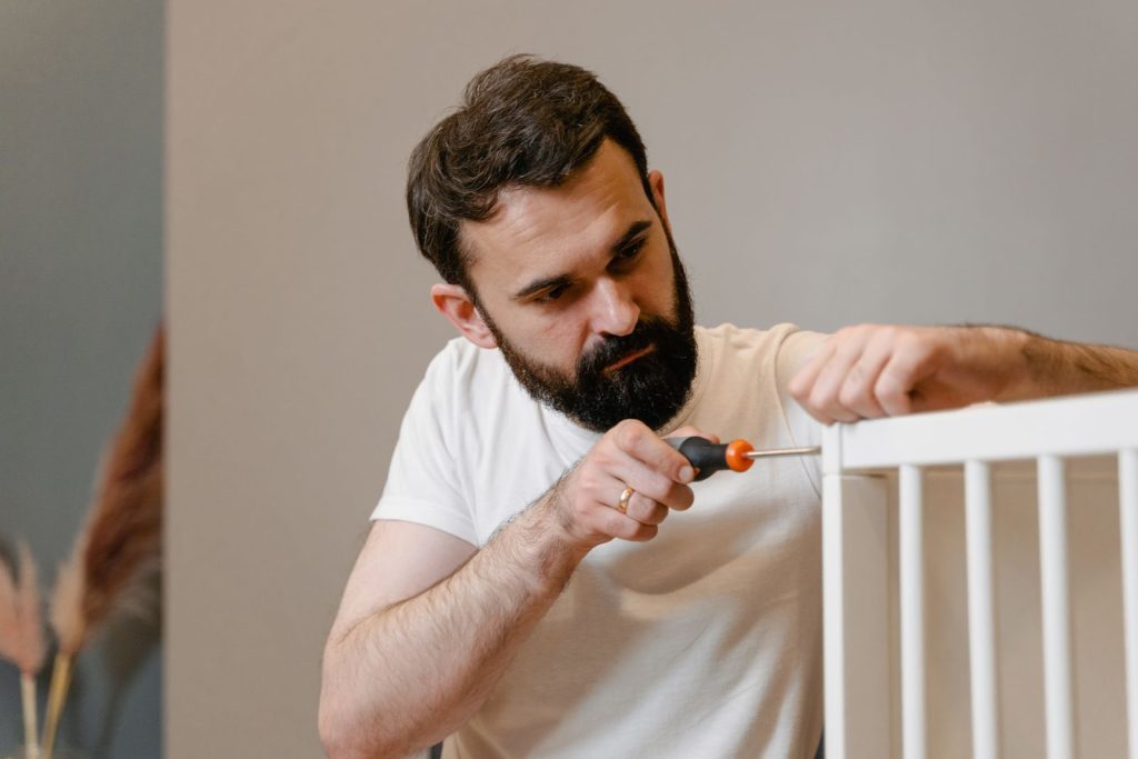 Man assembling a white crib with a screwdriver
