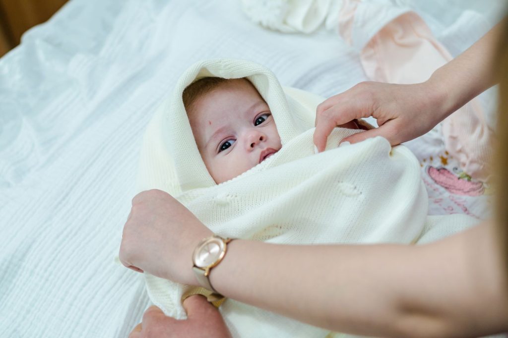 Adult hands wrapping a baby in a soft cream blanket